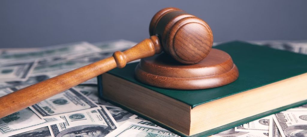 Photo of a gavel laying on top of a book, on top of a pile of 100 dollar bills