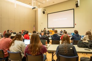 A photo of a USG Senate meeting taking place with 'Student Services' displayed as a presentation topic